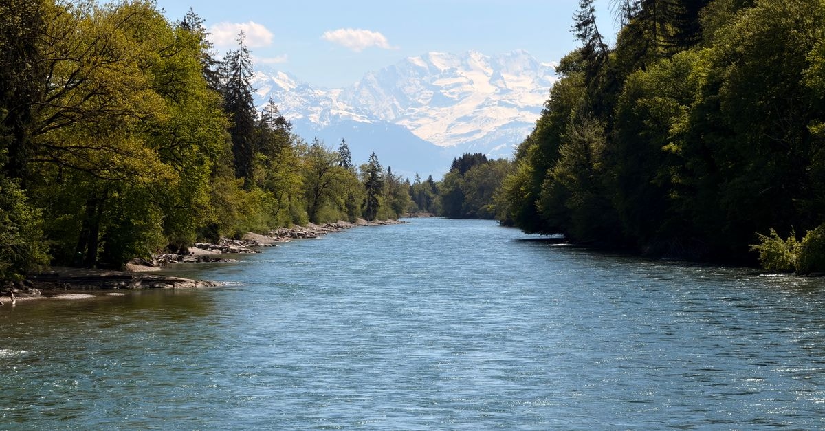 Slow Mornings and River Afternoons: A Bern Travel Guide Beautiful river flowing towards the Swiss Alps surrounded by lush greenery on a clear day.