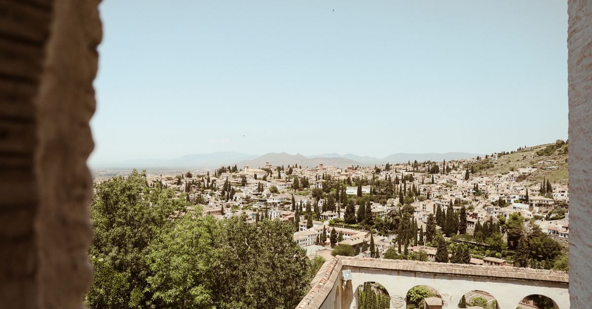 A Slow-Travel Guide to Granada, Spain Panoramic view of Granada cityscape framed by historic architecture under a summer sky.
