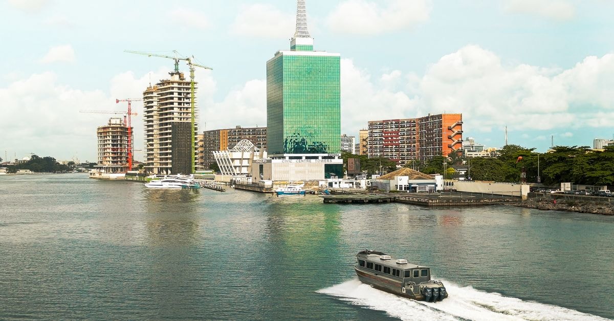 The Blowfish Hotel, Lagos: An Oasis-Style Boutique Stay in Victoria Island Scenic view of Lagos skyline featuring modern buildings and a motorboat in the lagoon under a bright sky.