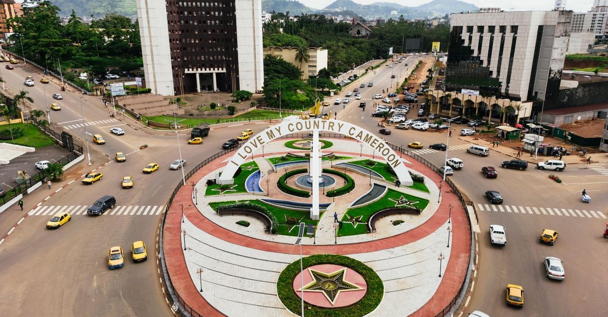 Kòló, Yaoundé: A Boutique Stay in Cameroon's Capital A vibrant aerial view of the 'Love My Country Cameroon' monument in Yaoundé, showcasing urban traffic and cityscape.